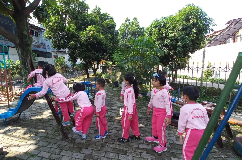 Belajar sabar dan berbagi giliran saat antre bermain perosotan dapat membantu mengembangkan kemampuan sosial-emosional siswa PAUD Asoka.